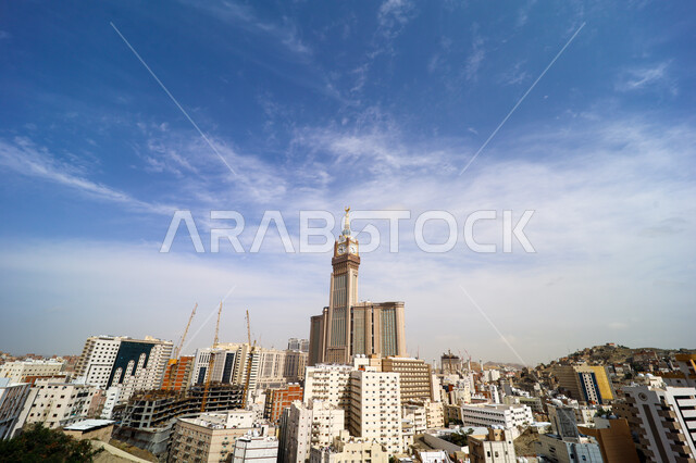 القمم والمرتفعات الجبلية، برج الساعه في مكة المكرمة في المملكة العربية السعودية, التضاريس والجبال والمناظر الطبيعية، المباني و البيوت السكنية في وقت النهار ,معالم اسلامية دينية مشهورة, خلفية السماء الزرقاء مع الغيوم البيضاء