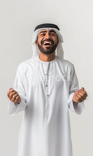 Expressions of pleasure and happiness, concern for external appearance, the concept of elegance and masculinity, a portrait of a Saudi Gulf Arab man wearing the traditional dress and shemagh, raising his hands with victory gestures, gray background