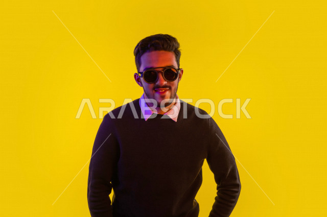 Portrait of a happy Saudi Gulf man, wearing sunglasses, different face and hands gestures indicating happiness and joy, vitality and entertainment, colorful background