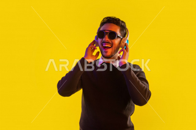 بورتريه رجل سعودي خليجي سعيد ، يضع سماعة رأس ، ايماءات وجه و يدين تدل على السعادة و الاستمتاع ، موهبة الغناء ، خلفية ملونة