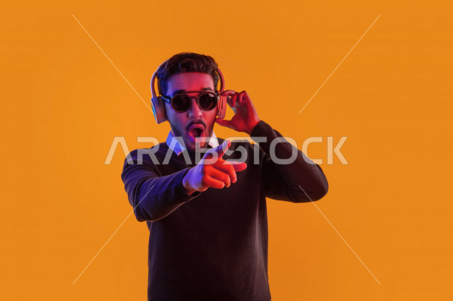 بورتريه رجل سعودي خليجي سعيد ، يضع سماعة رأس ، ايماءات وجه و يدين تدل على السعادة و الاستمتاع ، موهبة الغناء ، خلفية ملونة