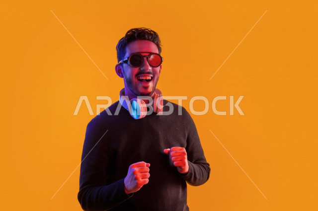 بورتريه رجل سعودي خليجي سعيد ، يضع سماعة رأس ، ايماءات وجه و يدين تدل على السعادة و الاستمتاع ، موهبة الغناء ، خلفية ملونة