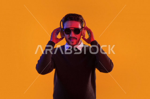 بورتريه رجل سعودي خليجي سعيد ، يضع سماعة رأس ، ايماءات وجه و يدين تدل على السعادة و الاستمتاع ، موهبة الغناء ، خلفية ملونة