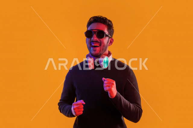 بورتريه رجل سعودي خليجي سعيد ، يضع سماعة رأس ، ايماءات وجه و يدين تدل على السعادة و الاستمتاع ، موهبة الغناء ، خلفية ملونة