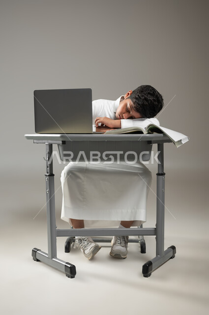 التعب بعد الجد والاجتهاد في الدروس, الحاجة إلى النوم والراحة, أهمية العلم والتعلم, بورتريه لطفل عربي خليجي سعودي يرتدي الثوب الأبيض التقليدي يجلس وينام في مقعده, دمج التكنولوجيا بالتعليم, استخدام تقنيات حديثة في التدريس, خلفية رمادية, محتوى حساس, استخدام حساس