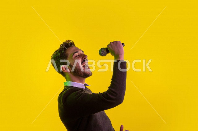 بورتريه رجل سعودي خليجي سعيد ،  يحمل الميكروفون و يقوم بالغناء  ، ايماءات وجه و يدين تدل على السعادة و الاستمتاع ، موهبة الغناء ، خلفية ملونة