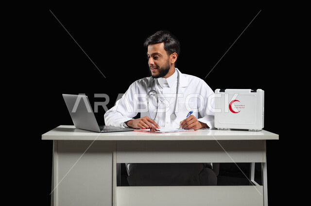 متابعة حالات المرضى عبر الاجهزة و التقنيات الحديثة, استخدام حقيبة الاسعافات الاوليه والحاسوب المحمول، بورتريه لطبيب عربي خليجي سعودي مبتسم يرتدي المعطف و السماعة الطبية يقوم بكتابة وتدوين التقارير والحالات الصحيه، خلفية سوداء, محتوى حساس, استخدام حساس