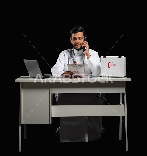 Providing medical consultations and diagnosing diseases through the technical device, a portrait of a young Saudi Arabian Gulf doctor wearing a medical coat and a stethoscope, making a call through a mobile phone, black background, sensitive use, sensitive content