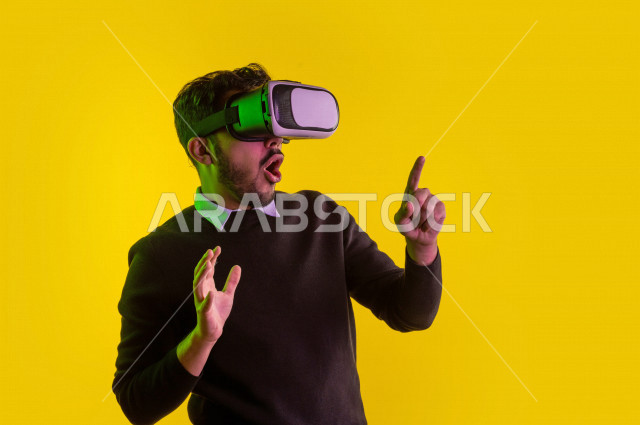 Portrait of a happy Saudi Gulf man, putting up a VR Box, face and hands gestures indicating happiness and enjoyment, using 3D technology, colored background