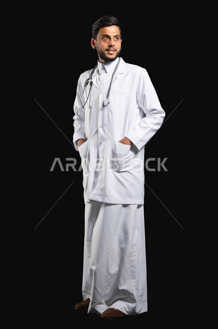 الوقوف باستقامة بايماءات الثقة، مفهوم الطب والرعايه الصحيه، ورتريه طبيب عربي خليجي سعودي يرتدي الزي التقليدي مع المعطف الطبي ينظر الى شيء ما معين، صورة الجسم بالطول الكامل، خلفية سوداء, محتوى حساس, استخدام حساس