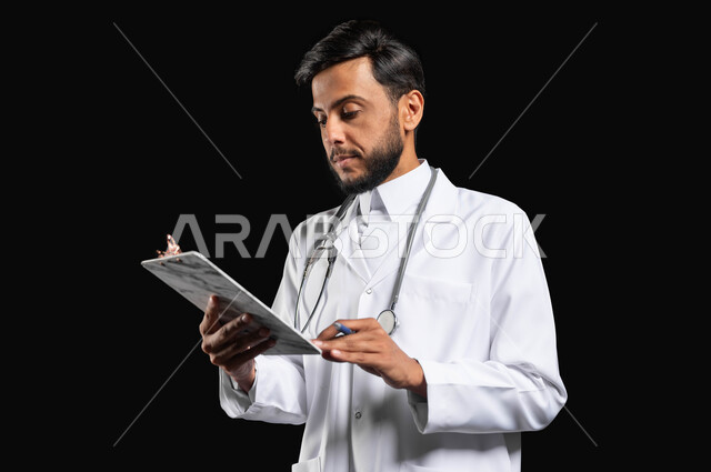 التعامل بتركيز وعناية مع تقارير المرضى، متابعة المرضى وتدوين حالاتهم المرضيه، بورتريه مقرب لطبيب عربي خليجي سعودي يرتدي المعطف و السماعة الطبية يقوم بمراجعة تقرير طبي، خلفية سوداء, محتوى حساس, استخدام حساس