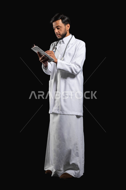 الاهتمام بالمرضى وتدوين الحالات المرضية، متابعه المرضى وتسجيل الملاحظات الطبيه، بورتريه طبيب عربي خليجي سعودي يرتدي الثوب التقليدي مع المعطف الطبي يقوم بتسجيل معلومات المرضى، صورة الجسم بالطول الكامل، خلفية سوداء, محتوى حساس, استخدام حساس