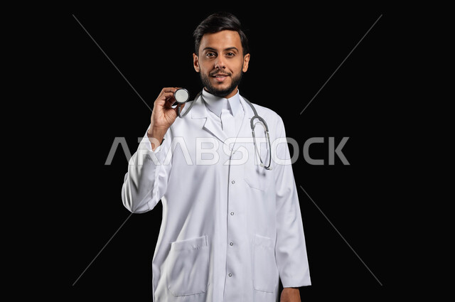 العمل في القطاع الطبي والرعايه الصحيه، استخدام السماعة الطبيه وتقديم الخدمات الطبيه، بورتريه ممرض عربي خليجي سعودي يرتدي المعطف الطبي ينظر الى الكاميرا بايماءات الرضا والسرور، خلفية سوداء, محتوى حساس, استخدام حساس