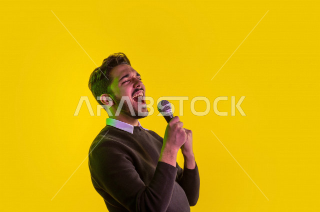 بورتريه رجل سعودي خليجي سعيد ،  يحمل الميكروفون و يقوم بالغناء  ، ايماءات وجه و يدين تدل على السعادة و الاستمتاع ، موهبة الغناء ، خلفية ملونة