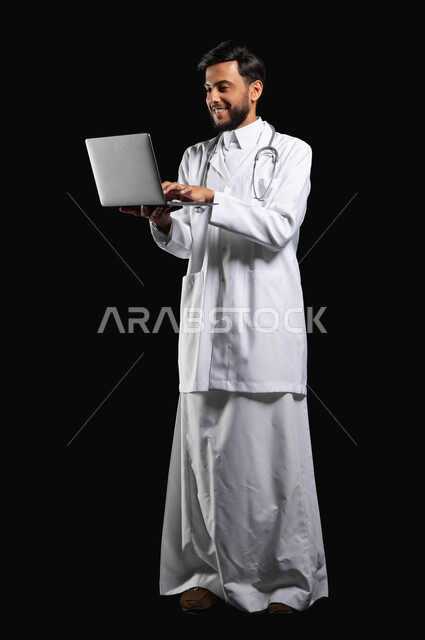 استخدام التقنيات الحديثة في المجال الطبي، متابعة الحالات المرضية من خلال الحاسوب المحمول، بورتريه طبيب عربي خليجي سعودي يستخدم الحاسوب المحمول، صورة الجسم بالطول الكامل، خلفية سوداء، محتوى حساس، استخدام حساس