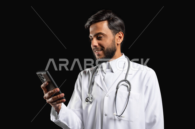 تلبية مطالب الرعاية الصحية عن بعد باستخدام التقنيات الحديثه، عرض خدمات و تطبيقات طبية عبر الهاتف، بورتريه مقرب لطبيب عربي خليجي سعودي يحمل بيده الهاتف المحمول، خلفية سوداء، محتوى حساس، استخدام حساس