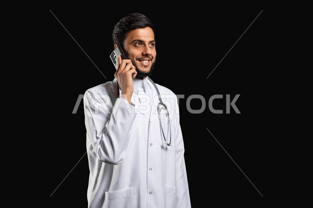 استخدام التقنيات الحديثه في مجال الطب، لتواصل مع المرضى عبر الهاتف المحمول, بورتريه مقرب لطبيب عربي خليجي سعودي مبتسم يرتدي المعطف الطبي يتكلم عبر الهاتف المحمول لتلبية مطالب الرعاية الصحية عن بعد، خلفية سوداء، استخدام حساس, محتوى حساس