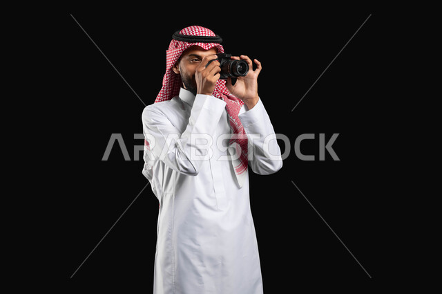 تنمية المواهب السعودية في مختلف المجالات, بورتريه لشاب عربي خليجي سعودي يرتدي الزي التقليدي والشماغ، يحمل بيده كامرا عالية الدقة ويلتقط الصور، احتراف الفوتوغراف، مصورين سعوديين ، كاميرات حديثة ومتطورة, استخدام التقنيات التكنولوجية في مجال التصوير