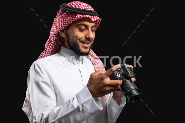 توثيق اللحظات السعيدة, بورتريه مقرب لشاب عربي خليجي سعودي يرتدي الزي التقليدي والشماغ، يحمل بيده كاميرا التصوير وينظر إلى الصور الملتقطة بإيمات السرور ، التصوير الفوتوغرافي ، موهبة واحتراف فن التصوير ، مصورين سعوديين ، تقنيات حديثة عالية الدقة