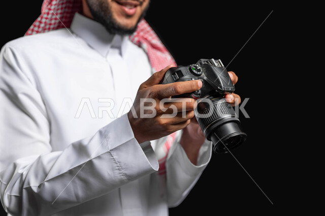 Photography using modern technologies, a close-up portrait of a Saudi Gulf Arab young man wearing a traditional dress and shemagh, holding a camera in his hand and looking at the captured images, photography, talent and professionalism in the art of photography, Saudi photographers, high-resolution cameras