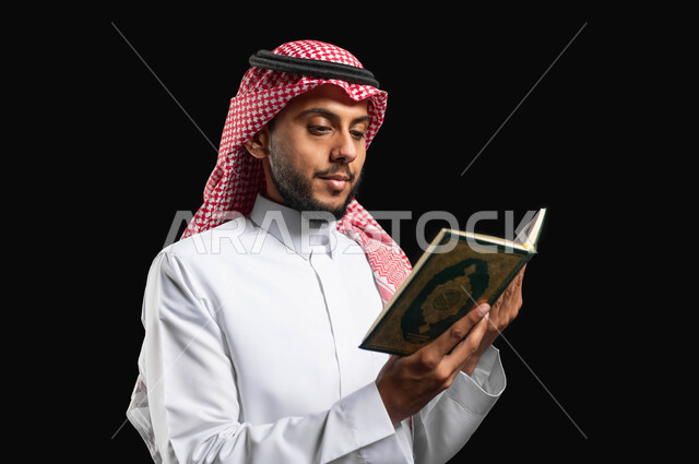 القيام بفرائض الإسلام, بورتريه مقرب بخلفية سوداء لرجل عربي سعودي خليجي يرتدي الثوب الأبيض التقليدي والشماغ السعودي, يحمل القرآن الكريم ويقرأ منه, تلاوة القرآن, الشعور بالخشوع والطمأنينه, الإكثار من ذكر الله تعالى, الإجتهاد في العباده, إسلاميات وعبادات