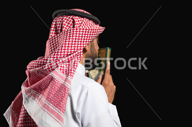 التقرب إلى الله العظيم, بورتريه  من الجانب لرجل عربي سعودي خليجي يرتدي الثوب الأبيض التقليدي والشماغ السعودي, يمسك القرآن الكريم بيديه ويقبله, الإكثار من ذكر الله تعالى, الإستغفار والدعاء, الإجتهاد في العبادة, خلفية سوداء