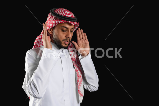 العبادة والتقرب إلى الله، الالتزام بأداء الفروض على وقتها، الركن الثاني من اركان الاسلام، بورتريه مقرب لرجل عربي خليجي سعودي مسلم يرتدي الثوب التقليدي والشماغ يقوم بالتكبير لبدء الصلاة، خلفية سوداء، استخدام حساس، محتوى حساس