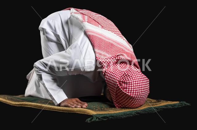 أداء الفرائض الدينية، الركن الثاني من اركان الاسلام، التقرب إلى الله عن طريق القيام يالعبادات، بورتريه مقرب لرجل عربي خليجي سعودي يرتدي الثوب التقليدي والشماغ يقوم بالسجود أثناء الصلاة، خلفية سوداء, استخدام حساس, محتوى حساس