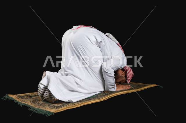 Getting closer to God by performing obligatory prayers and acts of worship, a portrait from the back of a Saudi Gulf Arab man wearing the traditional dress and shemagh, prostrating, performing the obligatory prayer on time, black background, sensitive use, sensitive content