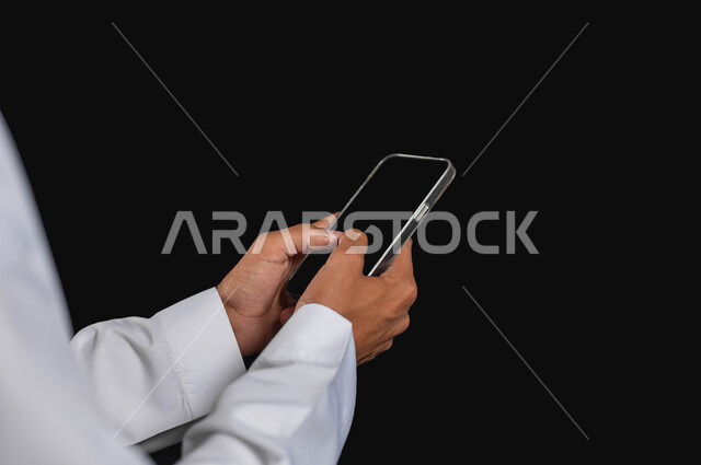 التطور والتكنولجيا واستخدام الهاتف المحمول، التواصل مع الاهل والاصدقاء، العمل عن بعد عبر الانترنت،بورتريه مقرب لرجل عربي خليجي سعودي يرتدي الزي التقليدي يحمل الهاتف المحمول،  خلفية سوداء، محتوى حساس، استخدام حساس