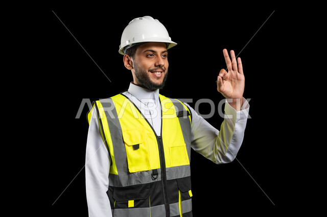مهن ووظائف هندسيه، الشعور بالقبول والموافقة والرضا، بورتريه لمهندس عربي خليجي سعودي يرتدي الزي التقليدي مع سترة الحمايه والخوذة يرفع يده للاعلى بايماءات علامة الجوده والرضى، صورة الجسم بالطول الكامل، خلفية سوداء, محتوى حساس، استخدام حساس