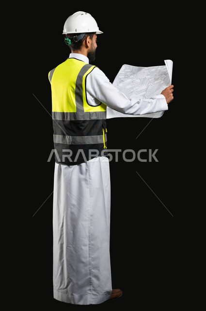 Project management and auditing, working in the engineering sector, portrait of a Saudi Arabian Gulf engineer wearing traditional clothing with a protective jacket and helmet reading project plans, full-length body image, sensitive content, sensitive use