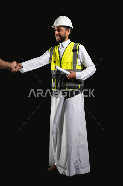 مهن ووظائف هندسية, اهمية التواصل مع العملاء في خدمة العمل، بورتريه لمهندس عربي خليجي سعودي يرتدي الزي التقليدي مع سترة الحماية والخوذة يحمل بيده مخططات المشروع، صورة الجسم بالطول الكامل، خلفية سوداء,محتوى حساس، استخدام حساس