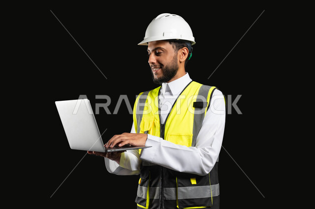 Working in the engineering sector, the concept of project management and auditing, a close-up portrait of a Saudi Gulf Arab engineer wearing traditional clothing working on a laptop, black background, sensitive content, sensitive use