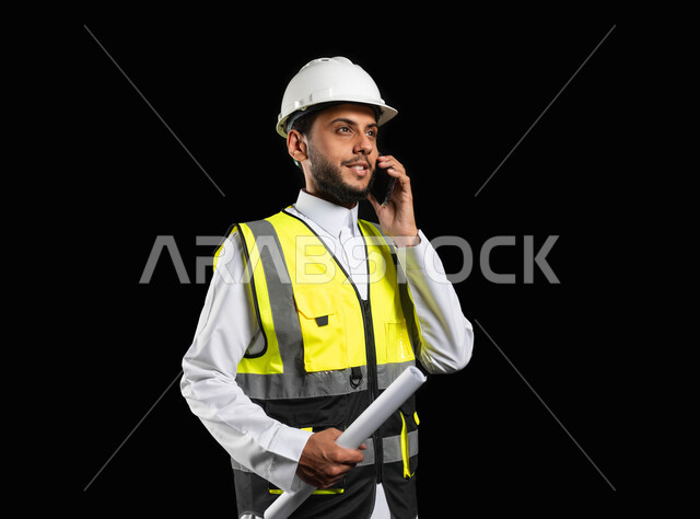 العمل في القطاع الهندسي، التواصل مع العملاء عبر الهاتف المحمول، بورتريه مقرب لمهندس عربي خليجي سعودي يرتدي الزي التقليدي مع سترة الحماية والخوذة يمسك بيديه مخططات المشروع، ادارة المشاريع وتدقيقها، مهن ووظائف هندسية, خلفية سوداء,محتوى حساس، استخدام حساس