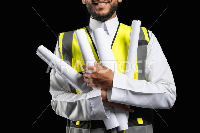 Working in the engineering sector, a close-up portrait of a Saudi Gulf Arab engineer wearing traditional clothing and a work protection jacket, holding project plans in his hands, project management and auditing, engineering professions and jobs, black background, sensitive content