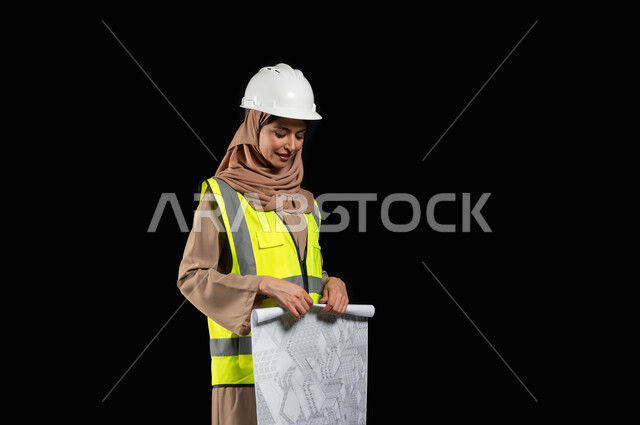 تقدم المشاريع الهندسية في السعودية,عمل النساء في القطاع الهندسي, التصاميم المعمارية وتدقيق المخططات, بورتريه لمهندسة عربية خليجية سعودية محجبة ترتدي سترة الحماية والخوذة تمسك مخطط الإعمار, مهن ووظائف نسائية, خلفية سوداء, محتوى حساس, استخدام حساس