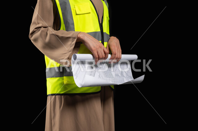 Developing engineering projects in Saudi Arabia, women working in the engineering sector, architectural designs and checking plans, portrait of a veiled Saudi Arabian Gulf engineer wearing a protective vest holding a reconstruction plan, women’s professions and jobs, black background, sensitive content, sensitive use