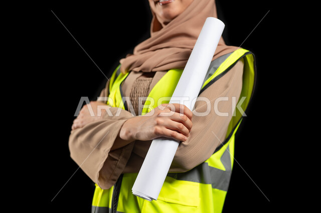 تطوير المشاريع الهندسية في المملكة العربية السعودية على يد أبنائها, بورتريه مقرب لمهندسة عربية خليجية سعودية محجبة ترتدي سترة و خوذة الحماية تحمل بيدها مخططات الاعمار, خلفية سوداء، استخدام حساس, محتوى حساس