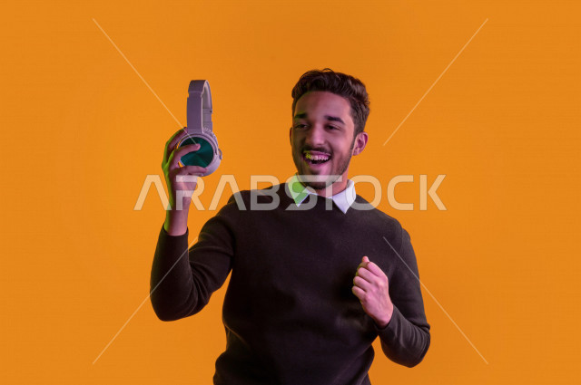 بورتريه رجل سعودي خليجي سعيد ، يضع سماعة رأس ، ايماءات وجه و يدين تدل على السعادة و الاستمتاع ، موهبة الغناء ، خلفية ملونة