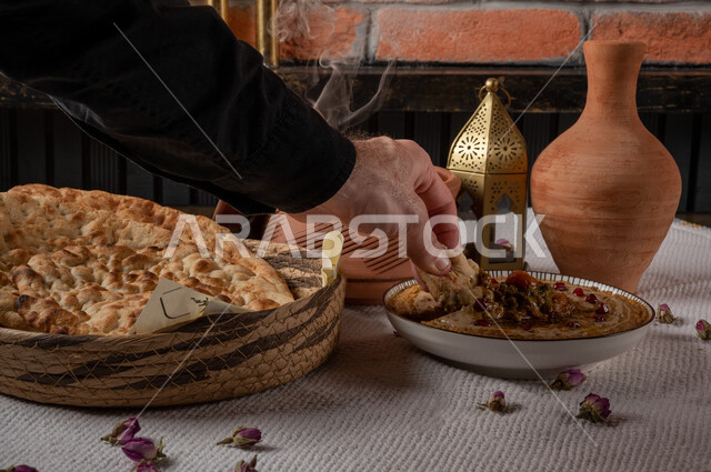مقبلات عربية باردة مع أواني فخارية، وجبة فطور صحية, مأكولات عربية تقليدية, أطعمة صحية غنية بالبروتينات, صورة مقربة ليد رجل عربي يأكل من احد طباق المتبل والفتات، أرغفة الخبز الطازجة