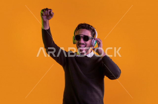 بورتريه رجل سعودي خليجي سعيد ، يضع سماعة رأس ، ايماءات وجه و يدين تدل على السعادة و الاستمتاع ، موهبة الغناء ، خلفية ملونة