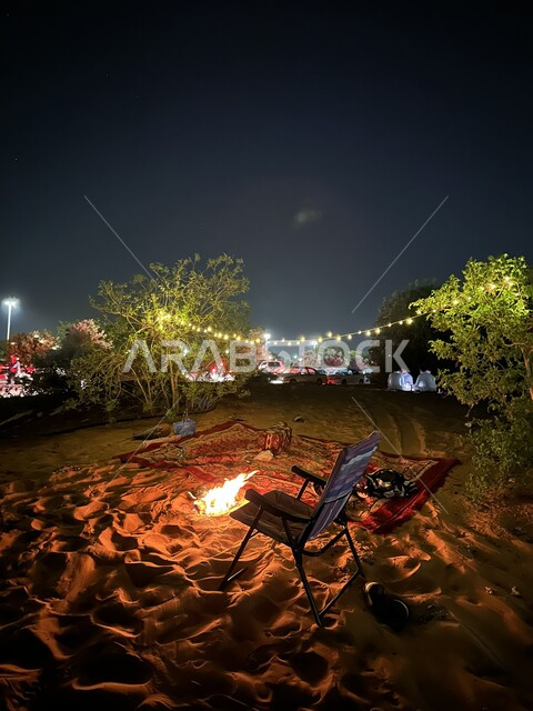 رحلة وكشتة برية في المناطق الصحراوية، الاستمتاع في الأجواء والجلسات الليلية الهادئة ، قضاء العطلة في براري المملكة العربية السعودية، شعلة من النار وسط الصحراء والأشجار الطبيعية الخضراء، الأضواء والأنوار في وقت الليل