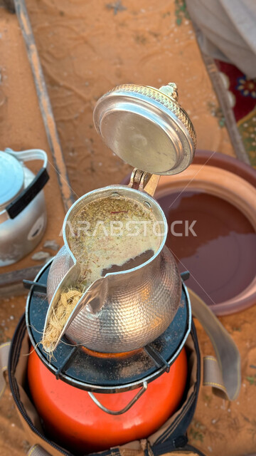 الاستمتاع بالمشروبات الساخنة في الشتاء البارد، صورة مقربة لدلة من القهوة على موقد نار مشتعل، كرم الضيافه وحسن الاستقبال، الكشتات البرية العربية الشعبية، أجواء التخييم في المناطق الصحراوية في المملكة العربية السعودية