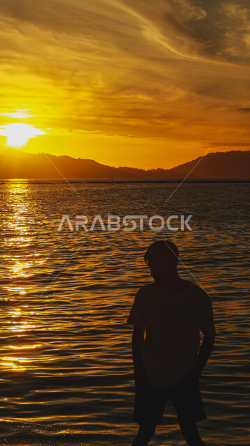 Trip and picnic areas in the summer, a view of the sunset over the sea coast, spending a pleasant time contemplating the tranquil landscape, a silhouette from the back of a Saudi Gulf Arab man standing on the sandy beach, natural places and the waterfront in the Kingdom of Saudi Arabia, Silhouette