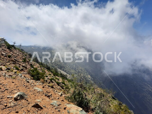 The view of white clouds in the summer atmosphere in Asir, the rocky mountain formations and formations in the city of Abha in the Kingdom of Saudi Arabia, cities and natural tourist places, the growth of wild herbs and green plants in the peaks and highlands.
