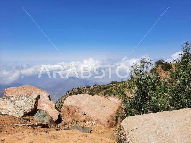 The growth of wild herbs and green plants in the peaks and highlands, the view of white clouds in the summer atmosphere in Asir, rocky mountain formations and formations in the city of Abha in the Kingdom of Saudi Arabia, cities and natural tourist places.
