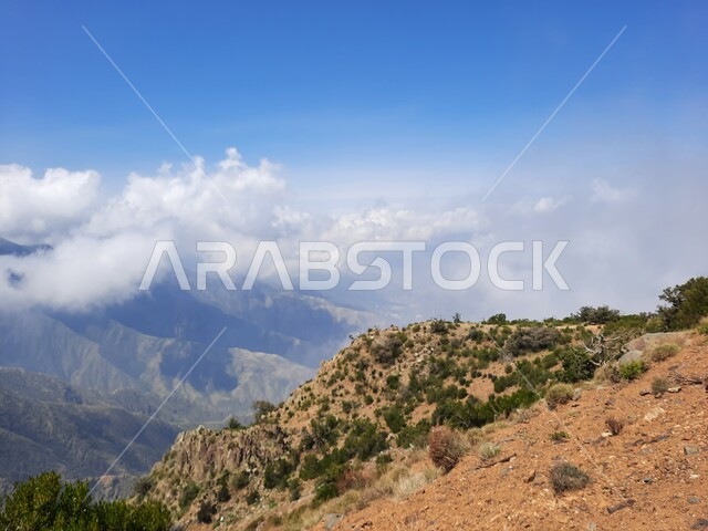 White clouds and clouds in the Asir sky, rocky mountain formations and formations in the city of Abha, cities and natural tourist places in the Kingdom of Saudi Arabia, the growth of wild herbs and green plants in the peaks and highlands.