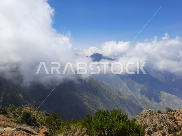 نمو الأعشاب البرية والنباتات الخضراء في القمم والمرتفعات، منظر الغيوم البيضاء في اجواء فصل الصيف في عسير، التكوينات والتشكيلات الجبلية الصخرية في مدينة ابها في المملكة العربية السعودية، مدن وأماكن سياحية طبيعية