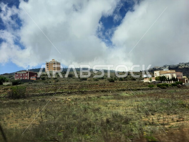 منظر السحب والغيوم البيضاء في السماء، القمم والمرتفعات الجبلية في مدينة ابها، مدن وأماكن سياحية طبيعية في المملكة العربية السعودية، القرى السكنية والبيوت والمنازل المبنية أعلى الجبل، الحقول والواحات الزراعية والنباتات الخضراء في جبال عسير